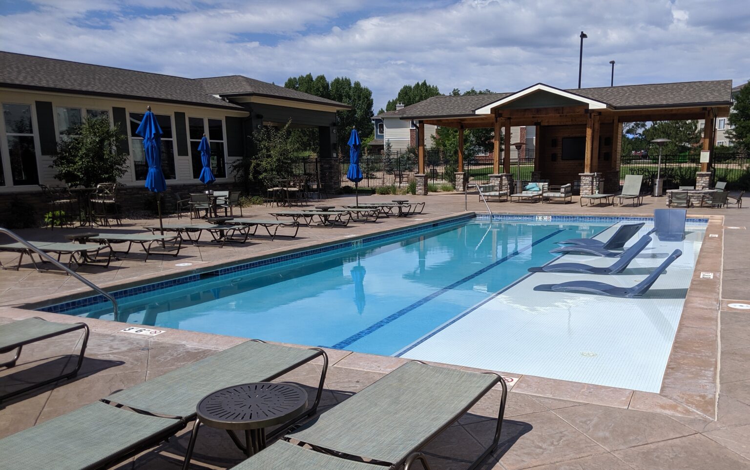 Outdoor swimming pool surrounded by lounge chairs and a shaded seating pavilion.